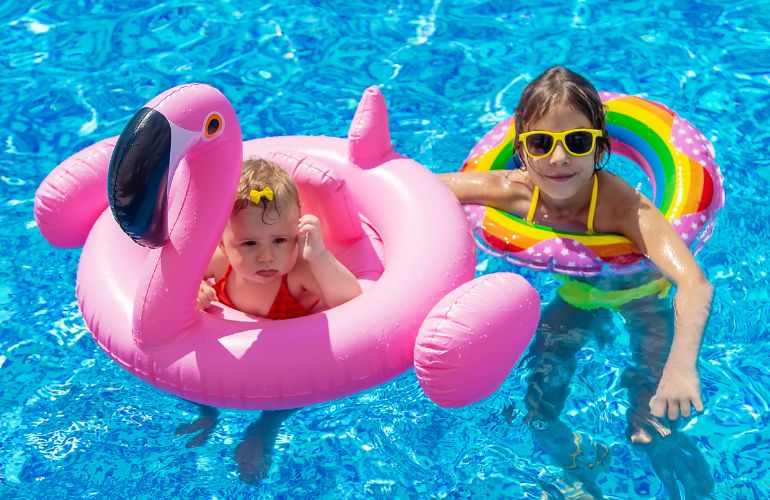 Dva deteta u bazenu plivaju uz pomoć šlaufa.
