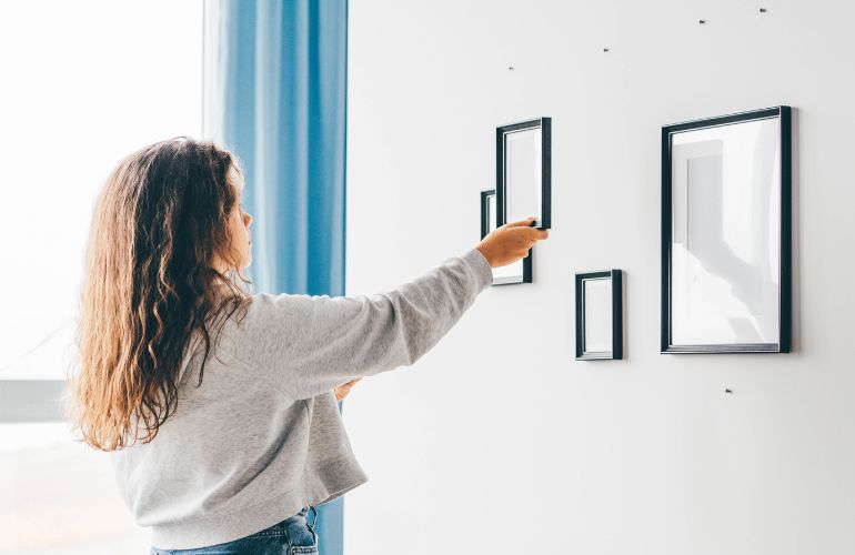 Devojka kači ramove za slike na zid.