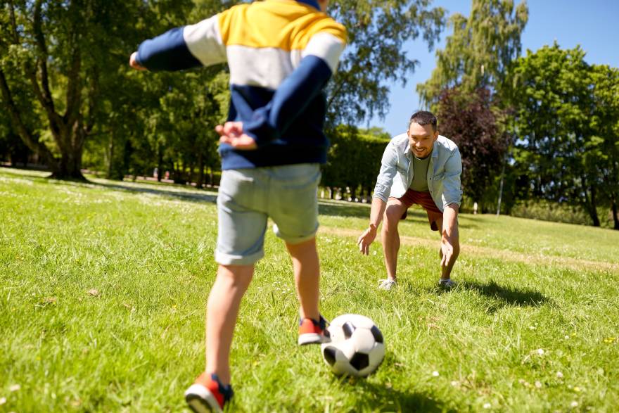 Otac igra fudbal sa sinom u parku